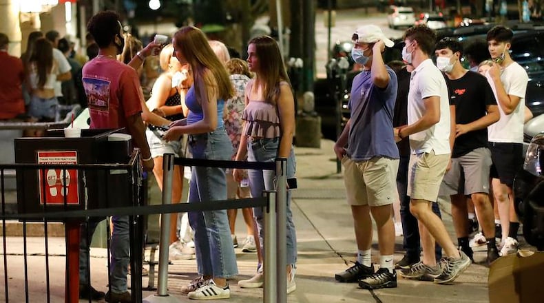 A doorman checks customers' temperatures as they wait in line to enter the Sandbar in downtown Athens. Bars will stop serving alcohol at 11:30 p.m. following a settlement reached Thursday between bar owners and county officials. (Joshua L. Jones/Athens Banner-Herald via AP)