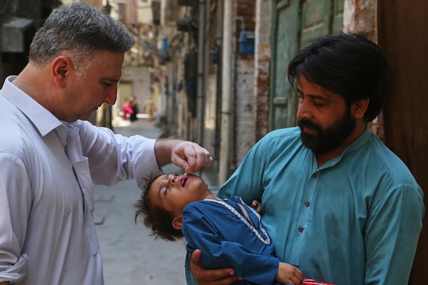 A health worker, left, administers a polio vaccine to a child at a neighborhood in Peshawar, Pakistan, Monday, May 26, 2025. (AP Photo/Muhammad Sajjad)