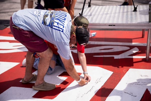 Fans sign the start/finish line at before a NASCAR Cup Series auto race at Darlington Raceway, Sunday, April 6, 2025, in Darlington, S.C. (AP Photo/Scott Kinser)
