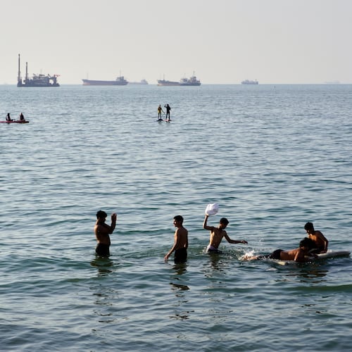 Residents swim and play in the waters of the Strait of Hormuz while cargo ships and commercial vessels lie anchored in the distance off Bandar Abbas, Iran, Wednesday, June 10, 2026.(Razieh Poudat/ISNA via AP)
