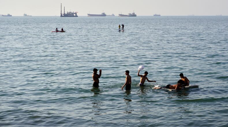 Residents swim and play in the waters of the Strait of Hormuz while cargo ships and commercial vessels lie anchored in the distance off Bandar Abbas, Iran, Wednesday, June 10, 2026.(Razieh Poudat/ISNA via AP)