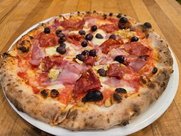 A pizza on a plate is topped with ham, salami, olives and artichokes