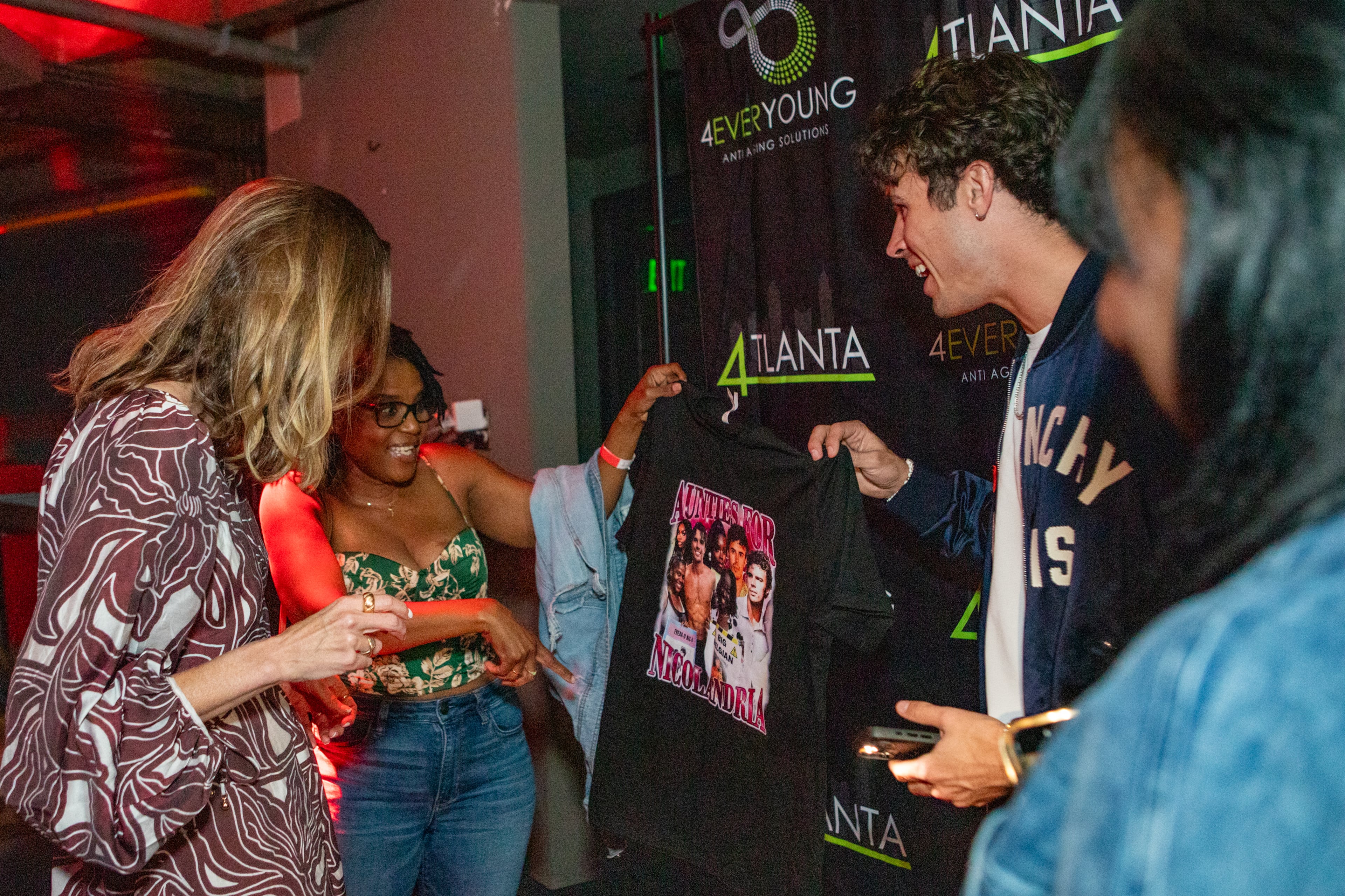 Nic Vansteenbergh (center), a breakout star from Love Island USA season 7 and one half of the popular "Nicolandria" couple, invites his mom over to see gifts from fans during the meet-and-greet at District Atlanta. (Jenni Girtman for the AJC)