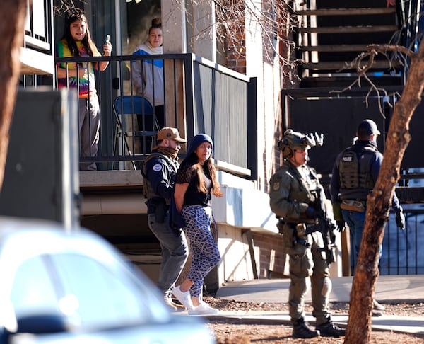 FILE - As a neighbor documents with a mobile telephone, a woman is escorted by a law officials from an apartment during a raid, Feb. 5, 2025, in east Denver. (AP Photo/David Zalubowski, File)