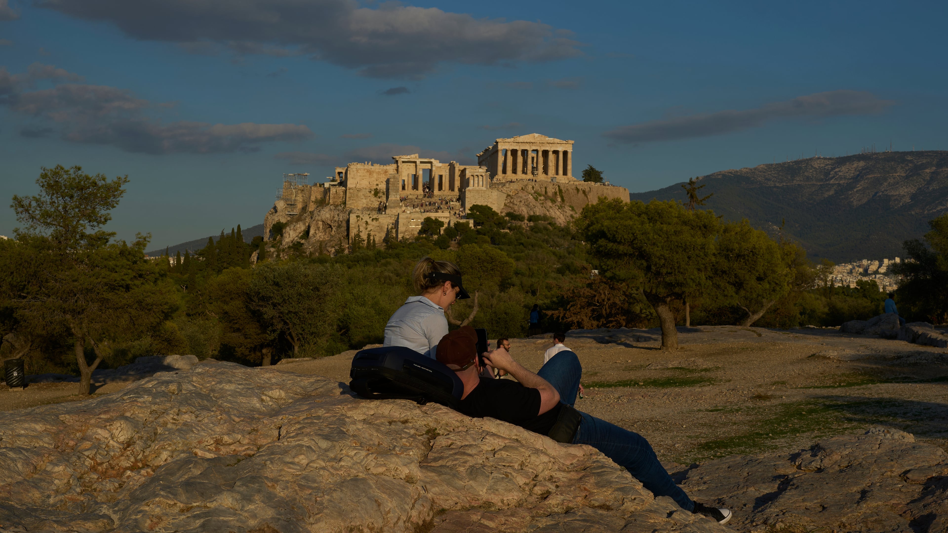 Tourist rest at Pnyx as the 5th century B.C. Parthenon temple stands free of scaffolding on the Acropolis hill in Athens, Friday, Oct. 10, 2025, after the removal of restoration structures that had covered parts of the ancient monument for decades.(AP Photo/Petros Giannakouris)