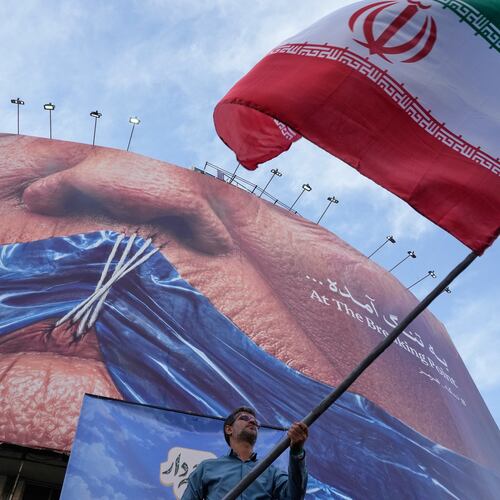 A man waves an Iranian flag for a pro-government campaign under a billboard with graphic showing Strait of Hormuz and sewn lips of U.S. President Donald Trump in a square in downtown Tehran, Iran, Wednesday, May 6, 2026. (AP Photo/Vahid Salemi)