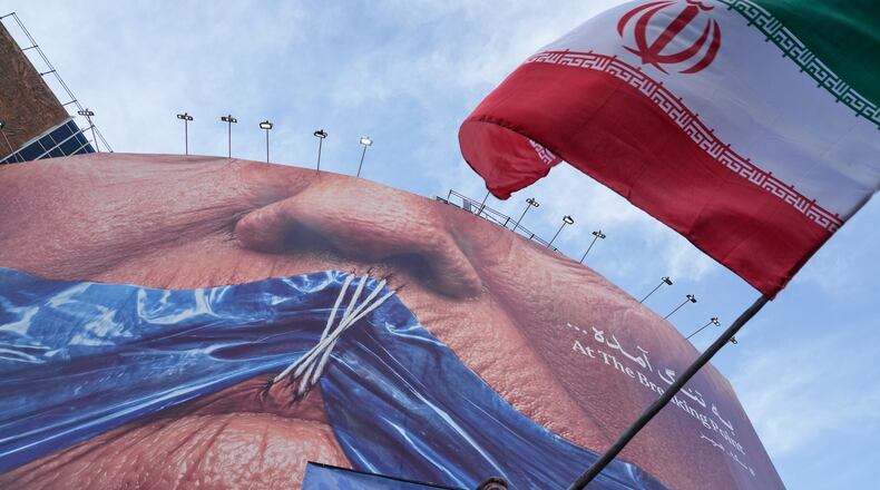 A man waves an Iranian flag for a pro-government campaign under a billboard with graphic showing Strait of Hormuz and sewn lips of U.S. President Donald Trump in a square in downtown Tehran, Iran, Wednesday, May 6, 2026. (AP Photo/Vahid Salemi)