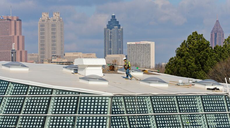 RAISING A REPTILE HOUSE--January 27, 2015 Atlanta: Against the Atlanta skyline - a worker crosses the roofline of the new Scaly Slimy Spectacular: The Amphibian and Reptile Experience, Tuesday, Jan. 27, 2015 at Zoo Atlanta. The $18-million complex will open this spring and be home to more than 60 animal species, including rare Cuban crocodiles. The 111,000 square-foot footprint will incorporate some 9,700 square feet of handcrafted rockwork; 60,000 gallons of water; and a 45-foot glass dome. JOHN SPINK/JSPINK@AJC.COM