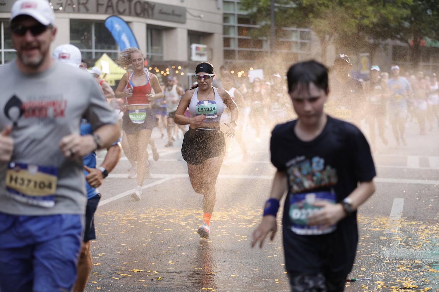 Water showers runners along Peachtree street at  the 56th running of the Atlanta Journal-Constitution Peachtree Road Race in Atlanta on Friday, July 4, 2025.   (Natrice Miller / AJC)