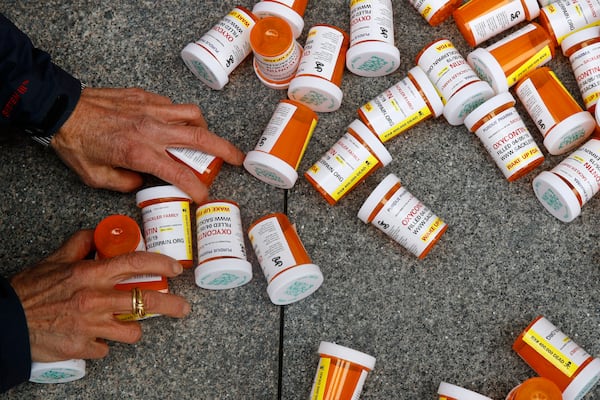 FILE - A protester gathers containers that look like OxyContin bottles at an anti-opioid demonstration in front of the U.S. Department of Health and Human Services headquarters in Washington on April 5, 2019. (AP Photo/Patrick Semansky, File)