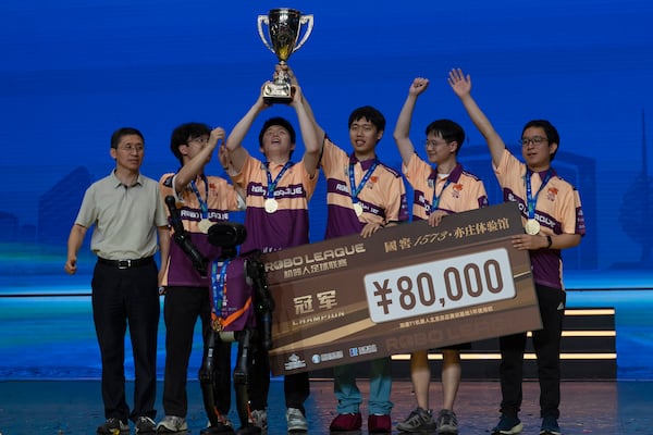 The human members of Team THU celebrate with their trophy near a T1 robot from Booster Robotics used during the inaugural RoBoLeague robot soccer competition held in Beijing, Saturday, June 28, 2025. (AP Photo/Ng Han Guan)