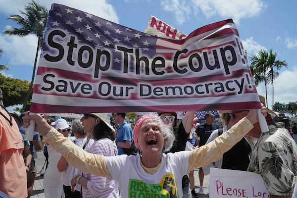 Protesters carry signs and chant slogans against the policies of President Donald Trump and Elon Musk Saturday, April 5, 2025, in Miami. (AP Photo/Marta Lavandier)