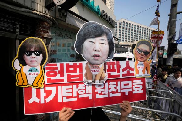 A supporter of impeached South Korean President Yoon Suk Yeol holds up a banner with images of the Constitutional Court of Korea's judges, from left Lee Mi-son, Chung Kye-sun and Moon Hyung-bae, near the Constitutional Court in Seoul, South Korea, Tuesday, April 1, 2025. The letters read "Fraudulent Impeachment is null and void." (AP Photo/Ahn Young-joon)