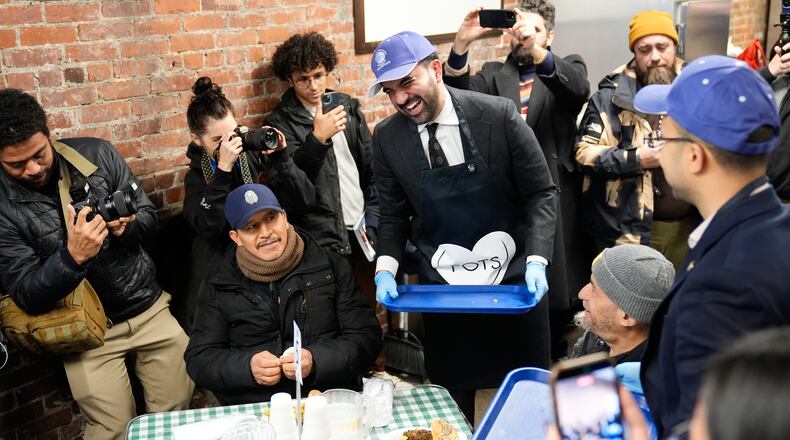 While surrounded by members of the media, New York City mayor-elect Zohran Mamdani, center, helps to serve meals at at POTS, a Bronx nonprofit that provides food assistance, in New York, Monday, Nov. 17, 2025. (AP Photo/Seth Wenig)