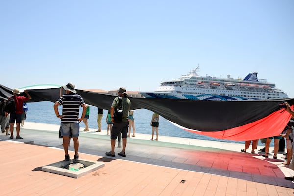 Protesters hold a Palestinian flag demonstrating as a cruise ship carrying Israeli tourists try to approach the Aegean Sea island of Syros, Greece, Tuesday, July 22, 2025. (Nikos Panagiotopoulos/InTime News via AP)
