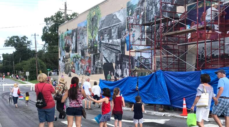 Passersby watch the work in progress of the Woodstock Community Mural. A ribbon-cutting to unveil the completed mural is set for 6 p.m. Saturday, July 21, in downtown Woodstock. WOODSTOCK COMMUNITY MURAL via Facebook