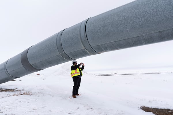 A worker takes a photo under the start of the Trans-Alaska Pipeline after a news conference at the Pump Station 1 on Monday, June 2, 2025, located near Deadhorse, Alaska, on the state's prodigious North Slope. (AP Photo/Jenny Kane)