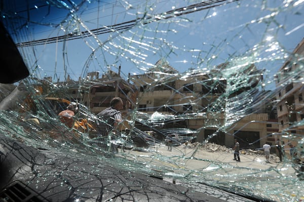 People seen through broken car window, as they gather in front of a destroyed building that was hit in an Israeli airstrike in Nabatieh town, south Lebanon, Friday, June 27, 2025. (AP Photo/Mohammed Zaatari)