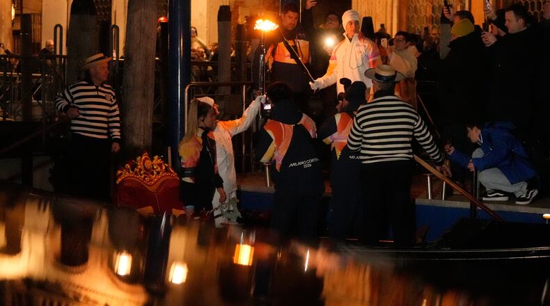 Torchbearers hold the Olympic torches flame on the Grand Canal in Venice, Italy, Thursday, Jan. 22, 2026, its journey will conclude in Milan on February 6 for the Winter Olympics opening ceremony. (AP Photo/Luca Bruno)