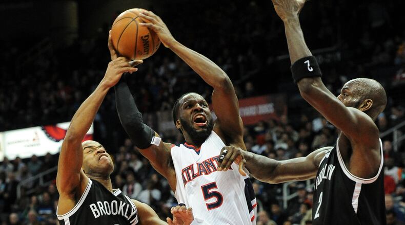 Atlanta Hawks forward DeMarre Carroll (5) shoots between the defense of Brooklyn Nets guard Jarrett Jack (0), and forward Kevin Garnett, right, during the first half of an NBA basketball game, Wednesday Jan. 28, 2015, in Atlanta. (AP Photo/John Amis)