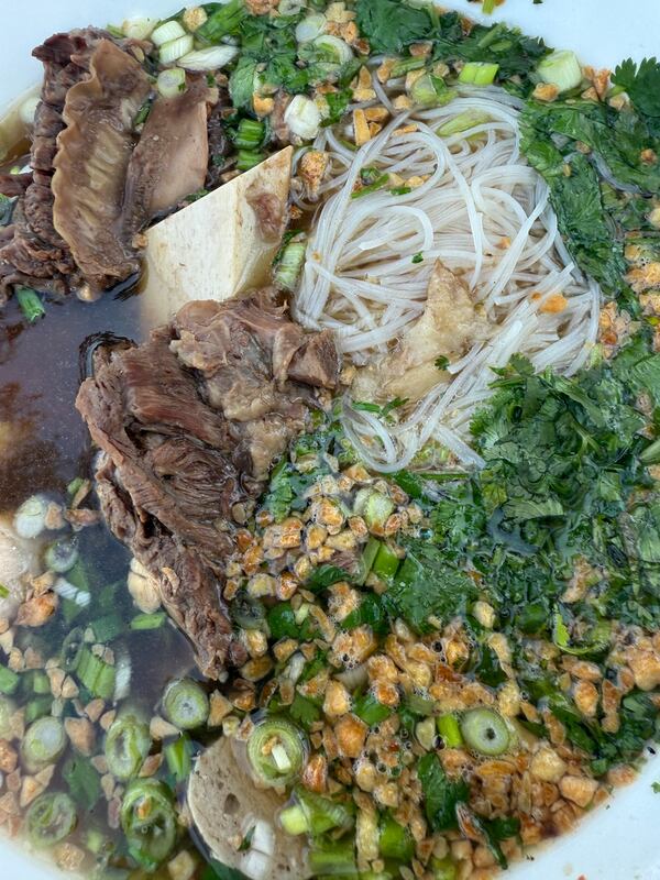 A close-up image of Cambodian pho soup, including generous amounts of meat, rice noodles, green onions and cilantro.