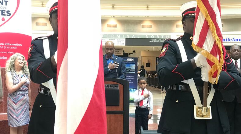 During the national anthem at a Hartsfield-Jackson Independence Day event on June 28, 2018, Simon Noellin, 5, is flanked by USO Georgia CEO Mary Lou Austin, left, Hartsfield-Jackson customer experience director Steve Mayers at the podium, and assistant general manager Richard Duncan, right.