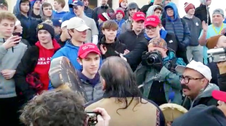 In this Friday, Jan. 18, 2019 image made from video provided by the Survival Media Agency, a teenager wearing a "Make America Great Again" hat, center left, stands in front of an elderly Native American singing and playing a drum in Washington. The Roman Catholic Diocese of Covington in Kentucky is looking into this and other videos that show youths, possibly from the diocese's all-male Covington Catholic High School, mocking Native Americans at a rally in Washington. (Survival Media Agency via AP)