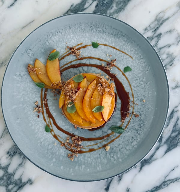 A plate containing.a peach tart surrounded by swirls of caramel and garnished with small pieces of fresh basil.