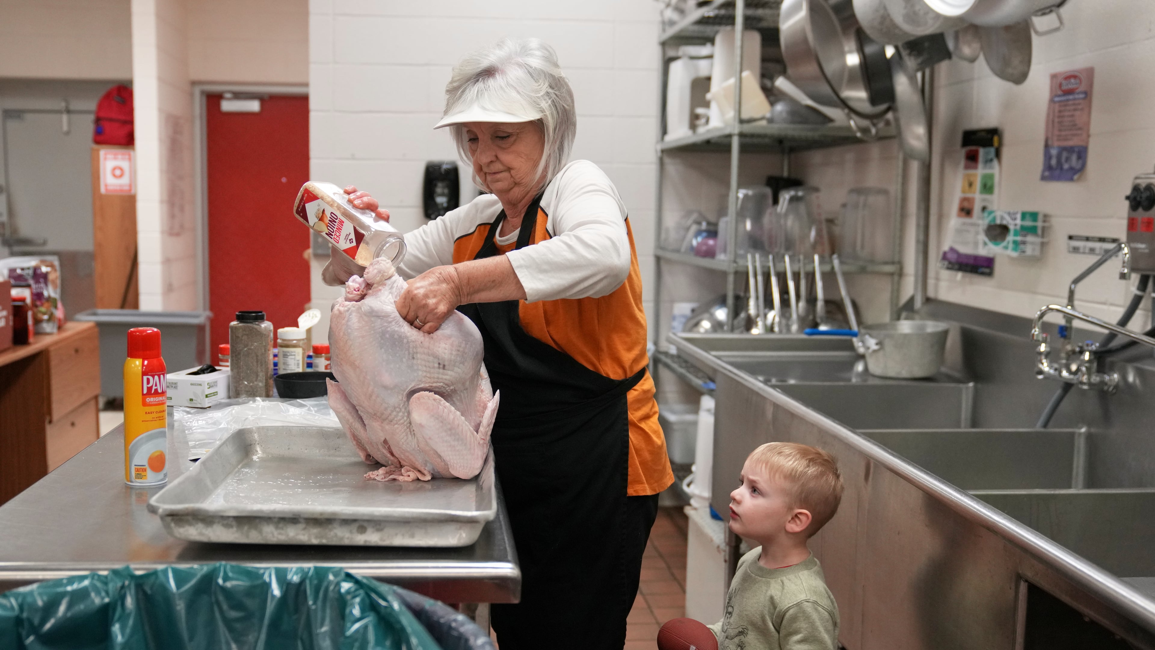 Kooper Keeland, 2, watches as his great-grandmother, high school cafeteria worker Shirley Mease, uses the kitchen at Reeds Spring High School to prepare 700 free Thanksgiving meals for community members Wednesday, Nov. 26, 2025, in Reeds Spring, Mo. (AP Photo/Jeff Roberson)