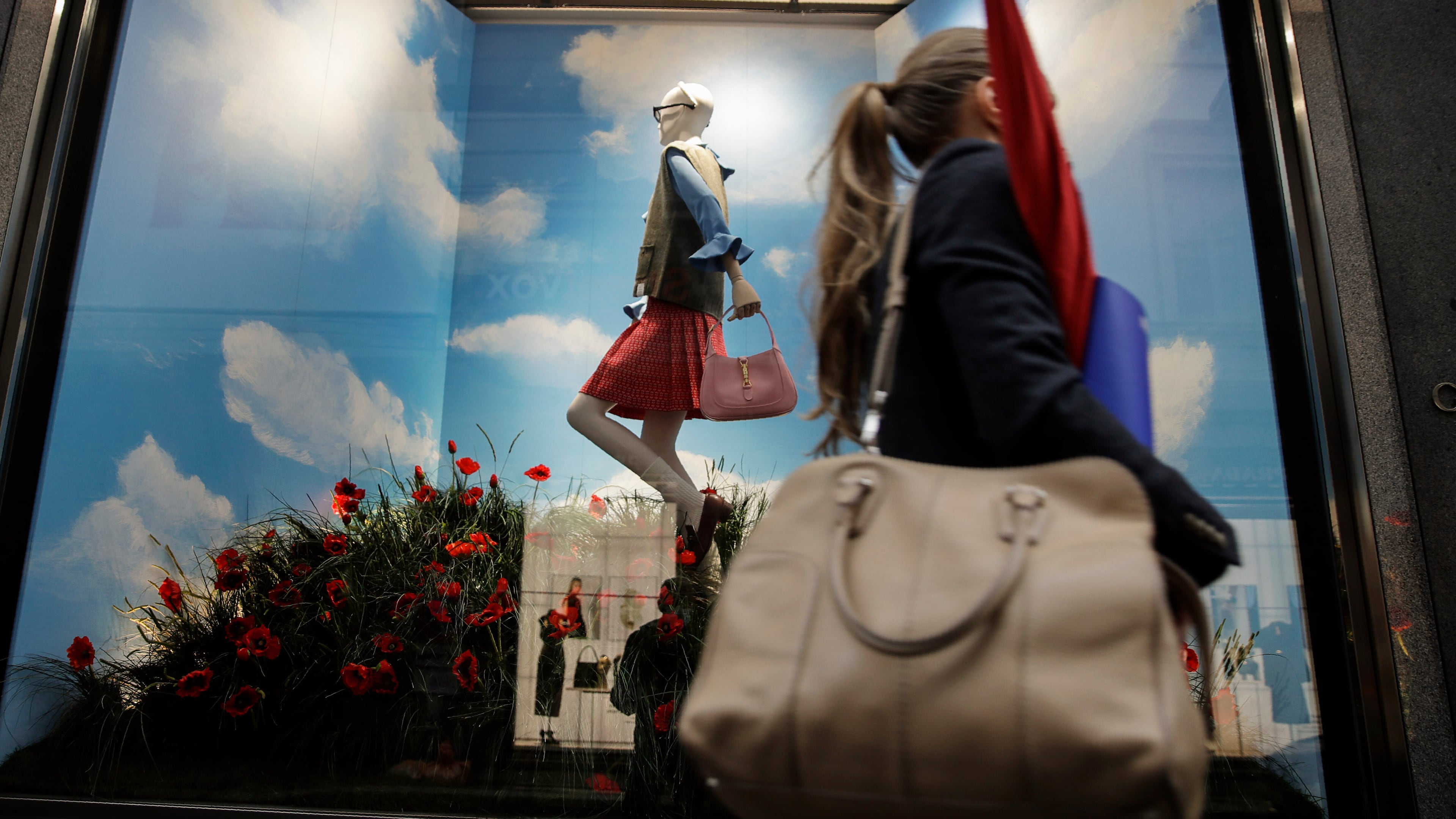 FILE - A woman walks past the Gucci store window at the Via Montenapoleone fashion district during Milan's fashion week in Milan, Italy, Sept. 25, 2020. (AP Photo/Luca Bruno, File)