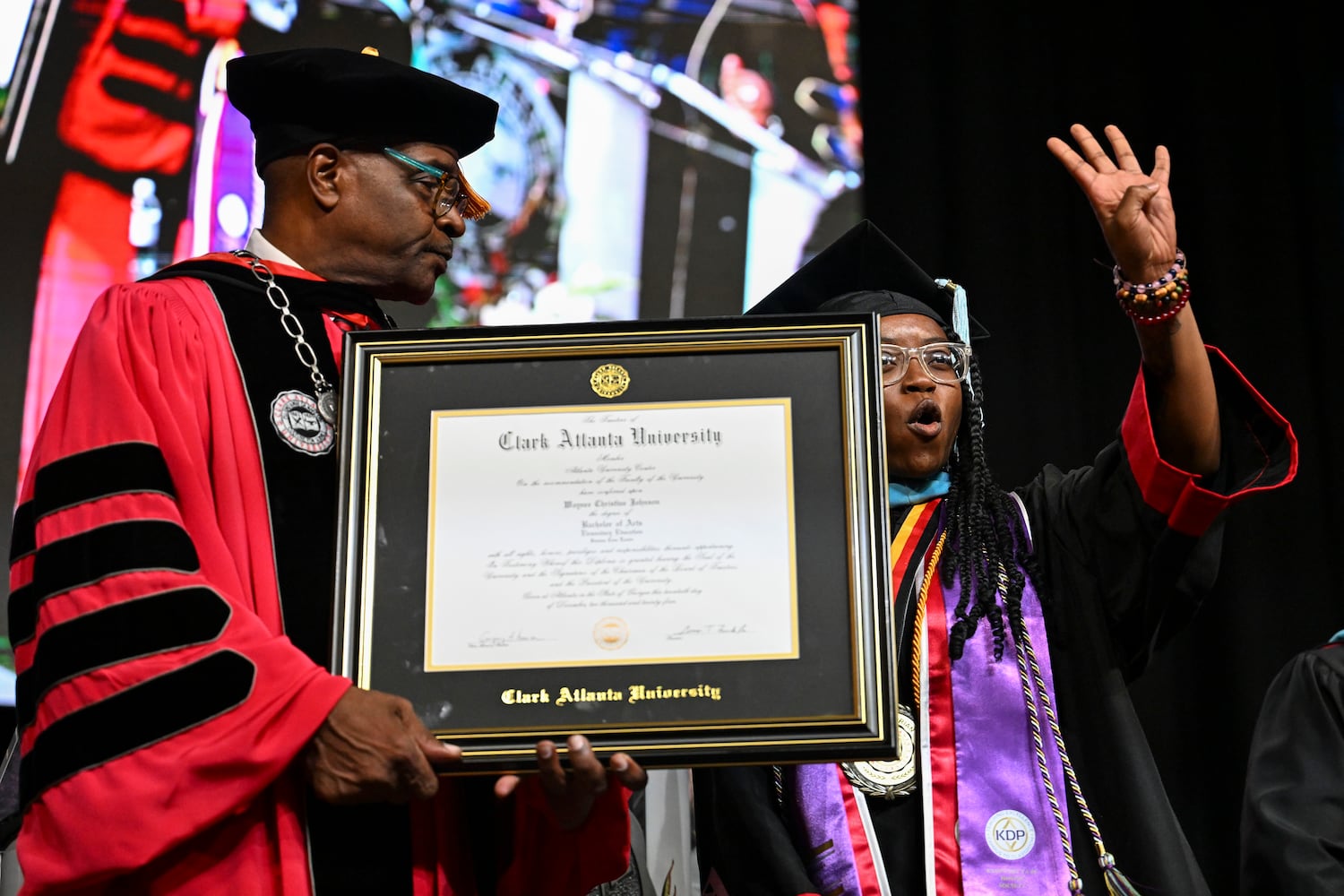 Valedictorian Waynee Christine Johnson gestures the number four, referencing her 4.0 GPA, as President George T. French Jr. looks on during Clark Atlanta University’s 2025 commencement ceremony Sunday, May 18, 2025 at Georgia State’s Convocation Center. (Daniel Varnado/For the Atlanta Journal-Constitution)