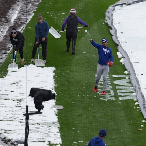 As the grounds crew works around him, Los Angeles Dodgers third baseman Santiago Espinal tosses a snowball at a coach while warming up to face the Colorado Rockies in a baseball game after a spring storm blanketed the intermountain West with a light covering of snow Friday, April 17, 2026, in Denver. (AP Photo/David Zalubowski)