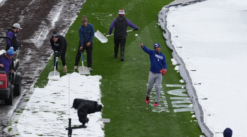 As the grounds crew works around him, Los Angeles Dodgers third baseman Santiago Espinal tosses a snowball at a coach while warming up to face the Colorado Rockies in a baseball game after a spring storm blanketed the intermountain West with a light covering of snow Friday, April 17, 2026, in Denver. (AP Photo/David Zalubowski)