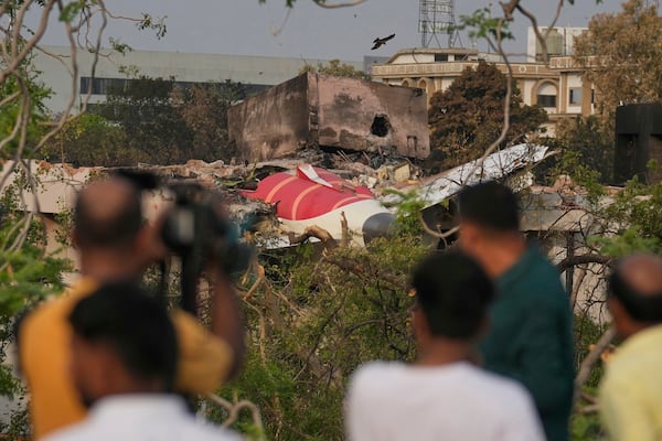 Onlookers watch wreckage from Thursday's Air India plane crash lying atop a building in Ahmedabad, India, Saturday, June 14, 2025. (AP Photo/Rafiq Maqbool)