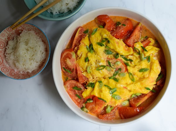 A serving bowl filled with Tomato and Egg Stir-Fry, shown with steamed white rice and chopsticks.