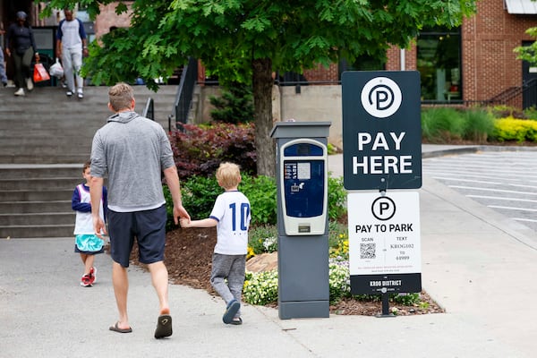 Visitors to the Krog Street Market District walk by signs indicating how to pay for parking outside the food hall. (Miguel Martinez/AJC)