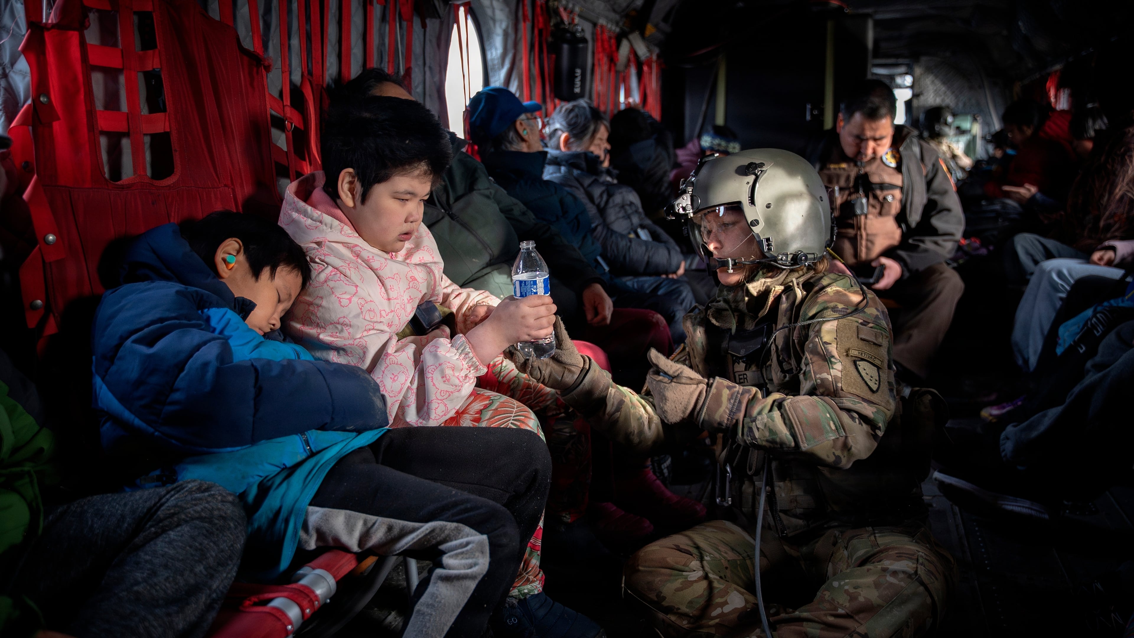 In this photo provided by the Alaska Army National, Guard Sgt. Mary Miller, a helicopter crew chief, passes a bottle of water to a child while evacuating displaced people from Kwigillingok, Alaska, during recovery operations on Thursday, Oct. 16, 2025. (Joseph Moon/Alaska National Guard via AP)