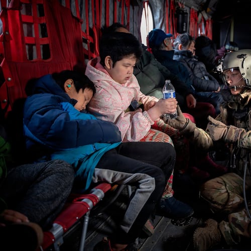 In this photo provided by the Alaska Army National, Guard Sgt. Mary Miller, a helicopter crew chief, passes a bottle of water to a child while evacuating displaced people from Kwigillingok, Alaska, during recovery operations on Thursday, Oct. 16, 2025. (Joseph Moon/Alaska National Guard via AP)