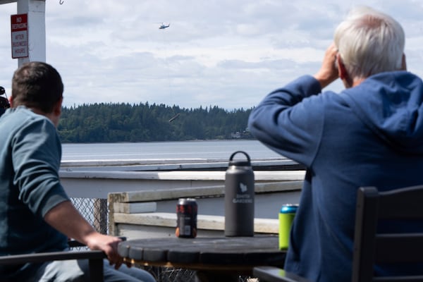 People watch as a helicopter carries an abandoned ship from Squaxin Island to shore on Wednesday, June 4, 2025, in Olympia, Wash. (AP Photo/Jenny Kane)