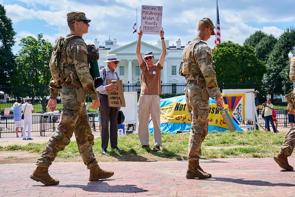 Members of the National Guard patrol Lafayette Park by the White House on Aug. 29, 2025. Holding up a sign, Will Roosien, of Grand Rapids, Michigan, says he hopes to inspire others of his generation to protest. (Jacquelyn Martin/AP)