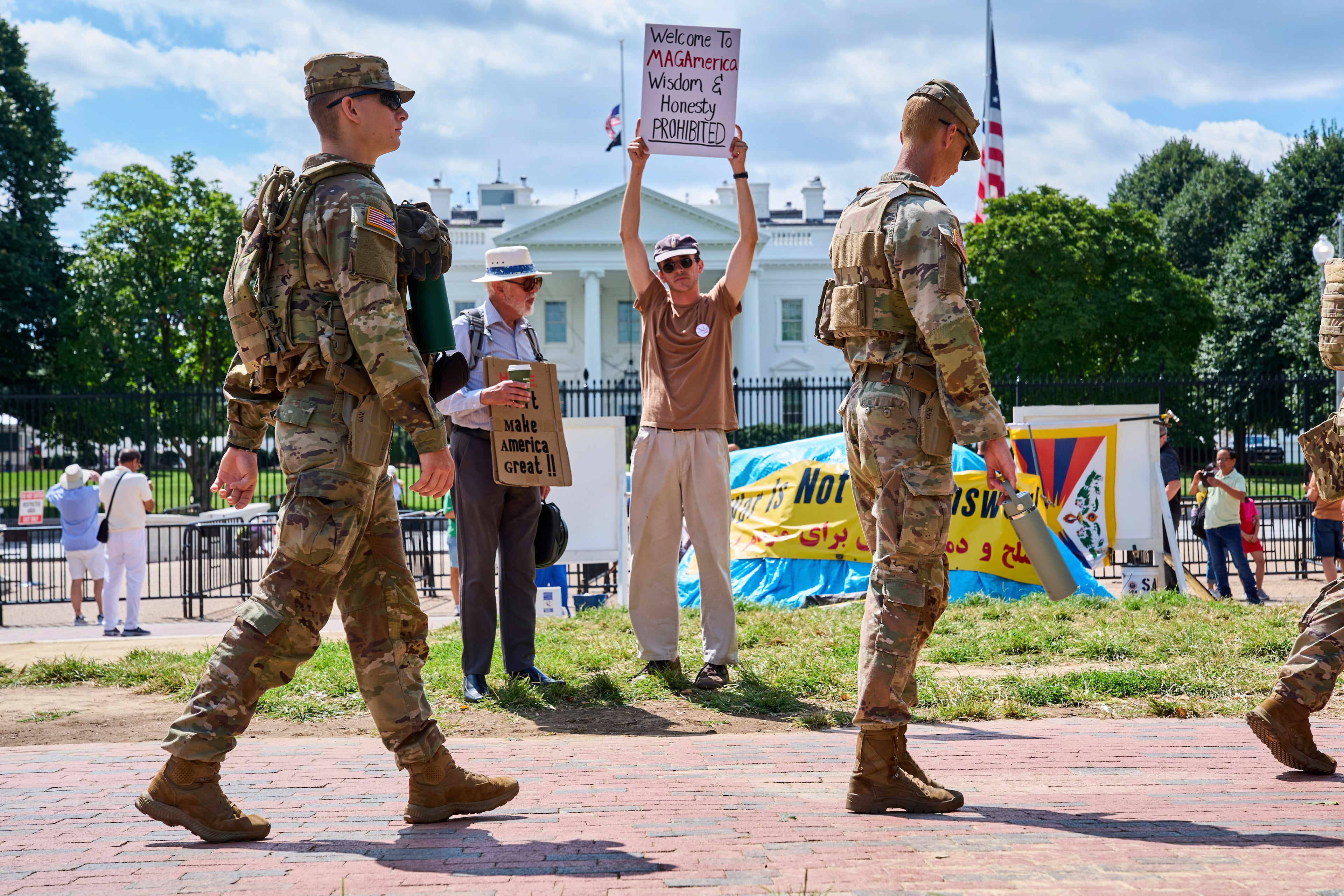 Members of the National Guard patrol Lafayette Park by the White House on Aug. 29, 2025. Holding up a sign, Will Roosien, of Grand Rapids, Michigan, says he hopes to inspire others of his generation to protest. (Jacquelyn Martin/AP)