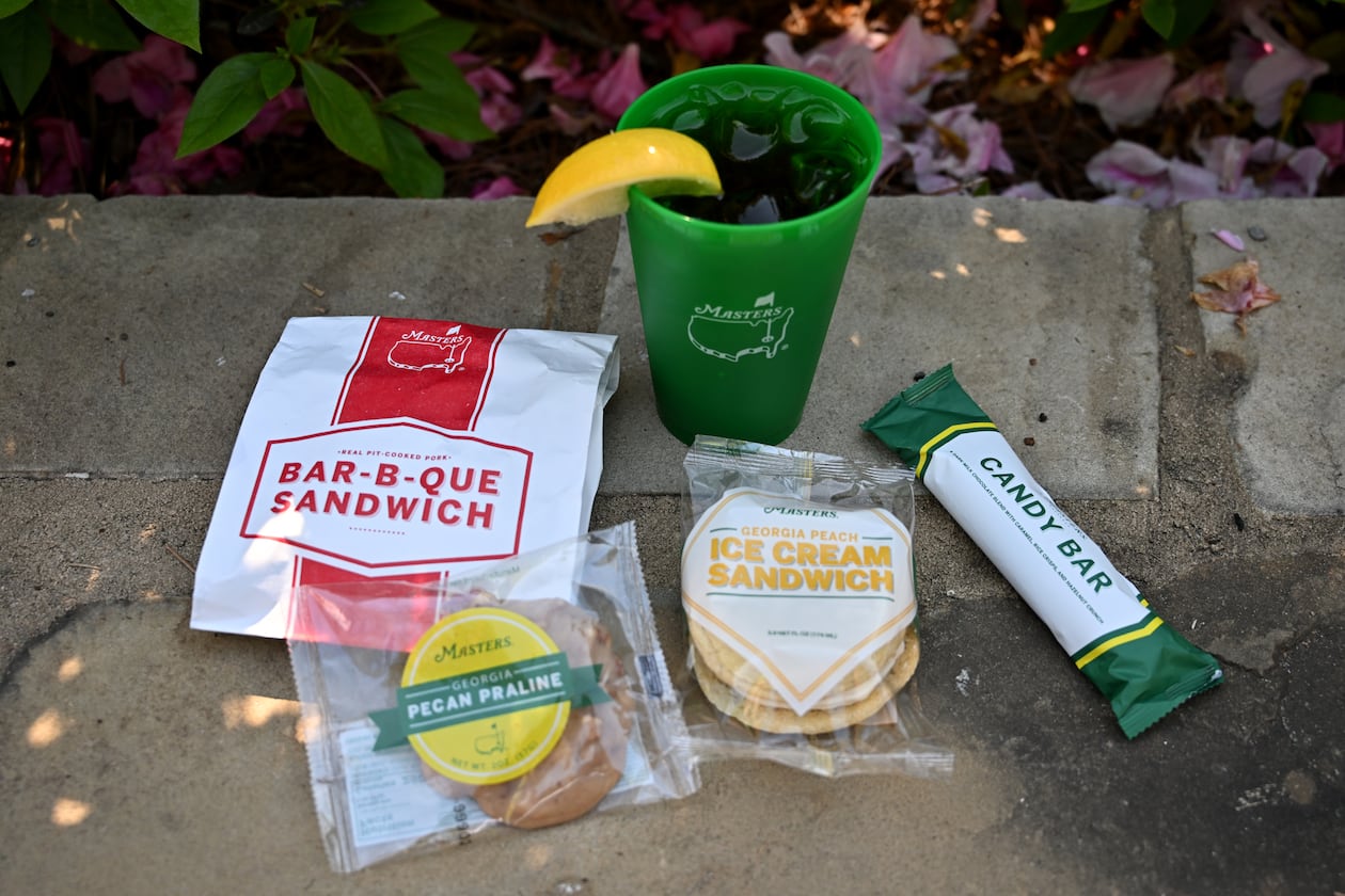Augusta National Golf Club’s food items include a pork bar-b-que sandwich (clockwise from left), ice tea, a Masters candy bar, a Georgia peach ice cream sandwich and a Georgia pecan praline. Augusta National is famous for its affordable, iconic concession menu. (Hyosub Shin/AJC)