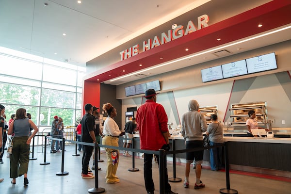 A line of people stands in front of a concession stand with red walls and a sign that says 'The Hangar'
