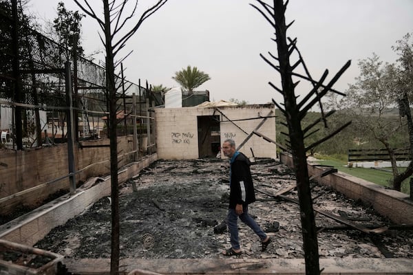 Mustafa Salama walks through the ruins of a wedding hall torched in an apparent settler attack in the West Bank town of Biddya, Tuesday, April 8, 2025. Hebrew graffiti: "fight the enemy not the lover," left, and "revenge," right. (AP Photo/Majdi Mohammed)