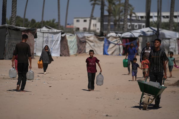 Palestinians carry containers for water at a camp for the displaced in Deir al-Balah, Gaza Strip, Monday, July 7, 2025. (AP Photo/Abdel Kareem Hana)