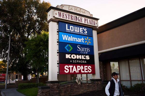 A person walks past a cluster of retail store signs in La Habra, Calif., Wednesday, April 2, 2025. (AP Photo/Jae C. Hong)