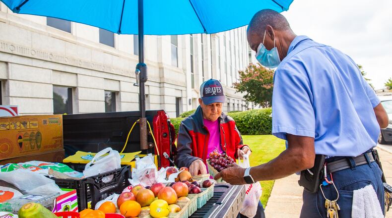 Gerald Reid, seated, who has been a mainstay for more than 50 years around the Atlanta state capitol campus, sells fresh fruits and vegetables out of the back of his truck to Eddie Ferrell, right, who works for the Georgia Building Authority, along Trinity Ave in Downtown Atlanta on Tuesday, Aug. 3, 2021. Reid, 79, comes downtown every week day from Fayetteville after a stop at his local farmers market to sells produce to those passing by, including Ferrell who is a regular customer and made note that Reid was missed on Monday, when he wasn't able to come. (Jenni Girtman for The Atlanta Journal Constitution)
