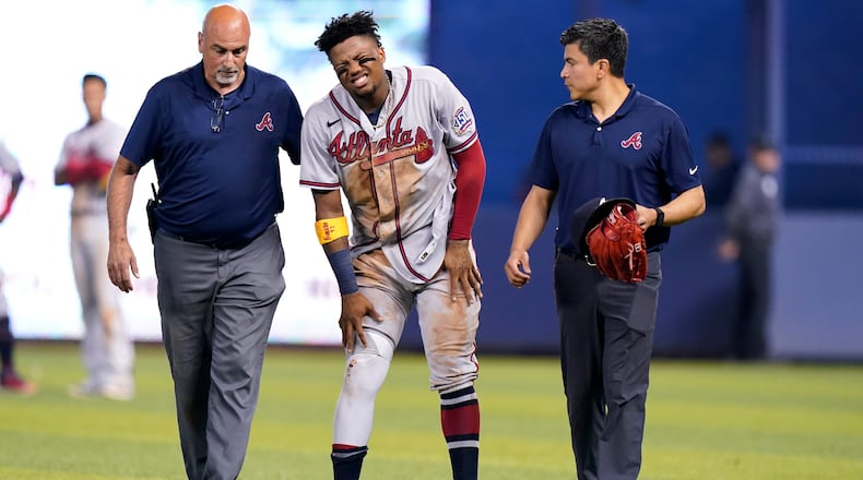 Atlanta Braves right fielder Ronald Acuna Jr., center, attempts to walk after trying to make a catch on an inside-the-park home run hit by Miami Marlins' Jazz Chisholm Jr. during the fifth inning of a baseball game, Saturday, July 10, 2021, in Miami.
