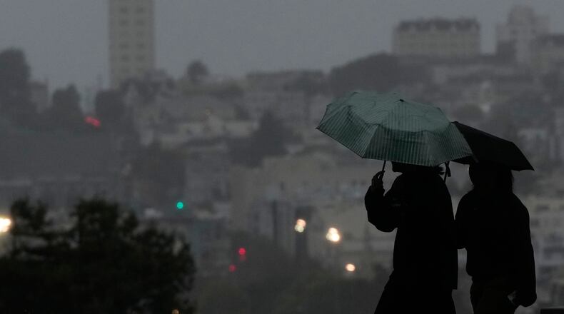 People carry umbrellas while walking on a path at Alamo Square Park, in San Francisco, Tuesday, Dec. 23, 2025. (AP Photo/Jeff Chiu)