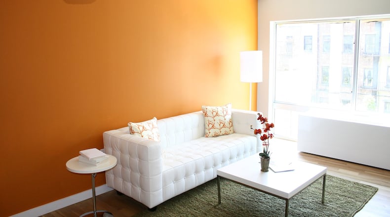 A rich orange accent wall serves as a backdrop in this minimal and modern living space. (Design Recipes)